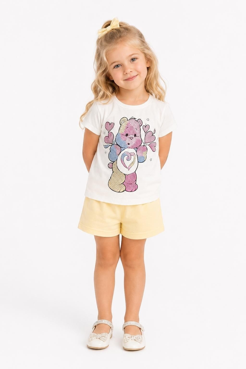 The Nile Luxuries girl wearing a white Care Bears graphic t-shirt and yellow shorts with a matching hair bow.