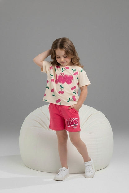 Girl wearing The Nile Luxuries cream cherry-print t-shirt and pink shorts with LOVE graphic on a beanbag chair.