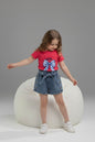 Girl wearing The Nile Luxuries red ribbed top with bow graphic and denim paper-bag waist shorts with side buttons.