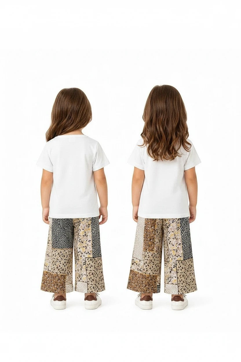 Two young girls wearing The Nile Luxuries white t-shirts and wide-leg patchwork floral trousers from the back.