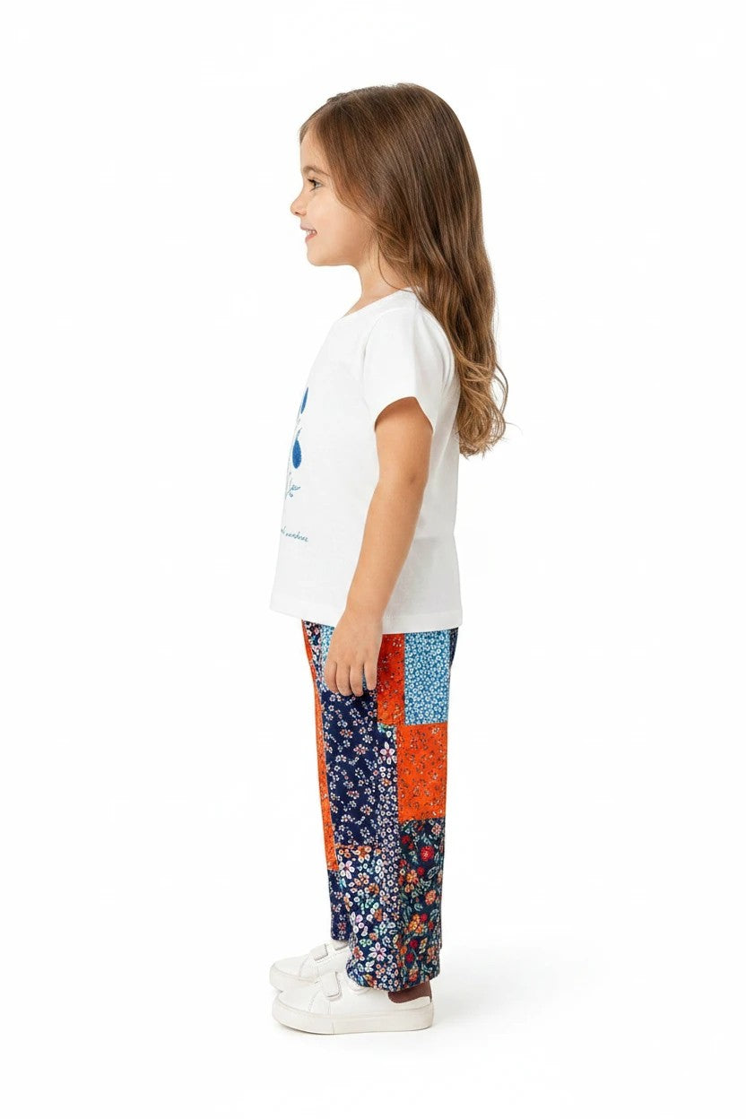 Young girl wearing The Nile Luxuries white graphic t-shirt and vibrant patchwork floral wide-leg pants with sneakers.