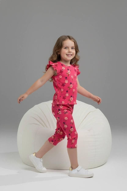 Young girl wearing a pink floral ribbed lounge set with flutter sleeves by The Nile Luxuries, paired with white shoes.
