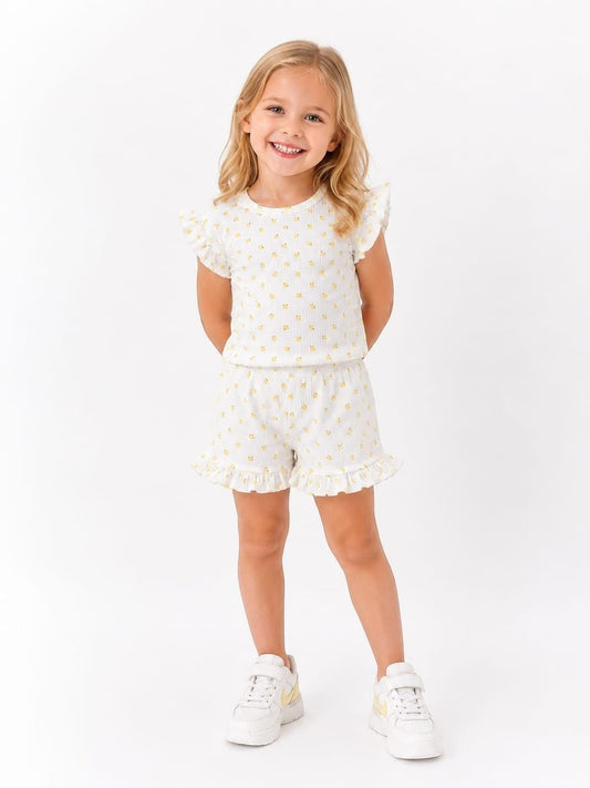 A young girl smiling in The Nile Luxuries white floral ruffle short sleeve top and matching shorts lounge set.