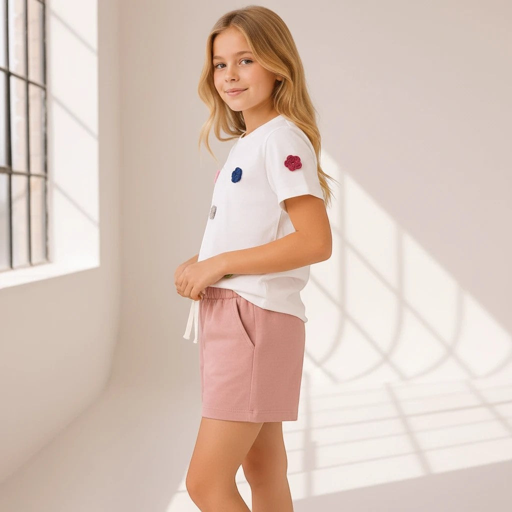 The Nile Luxuries girls' white t-shirt with floral crochet appliqués and dusty-rose knit shorts with side pockets.