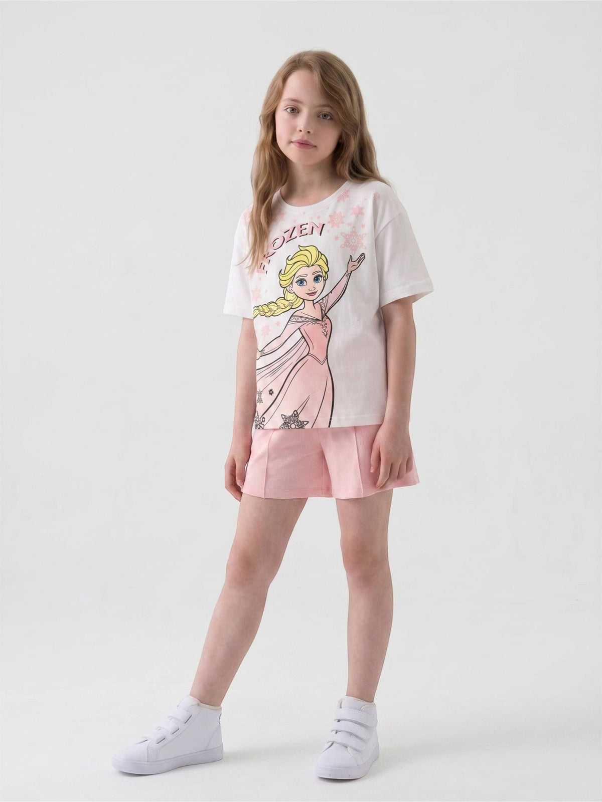 Girl wearing The Nile Luxuries white Frozen graphic t-shirt and pink shorts with white sneakers against white background