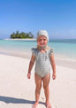 The Nile Luxuries girls' blue and cream gingham ruffle sleeve swimsuit and matching bonnet on a beach.