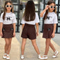 The Nile Luxuries girls outfit set with white graphic t-shirt and brown pleated skirt featuring black bow accents.