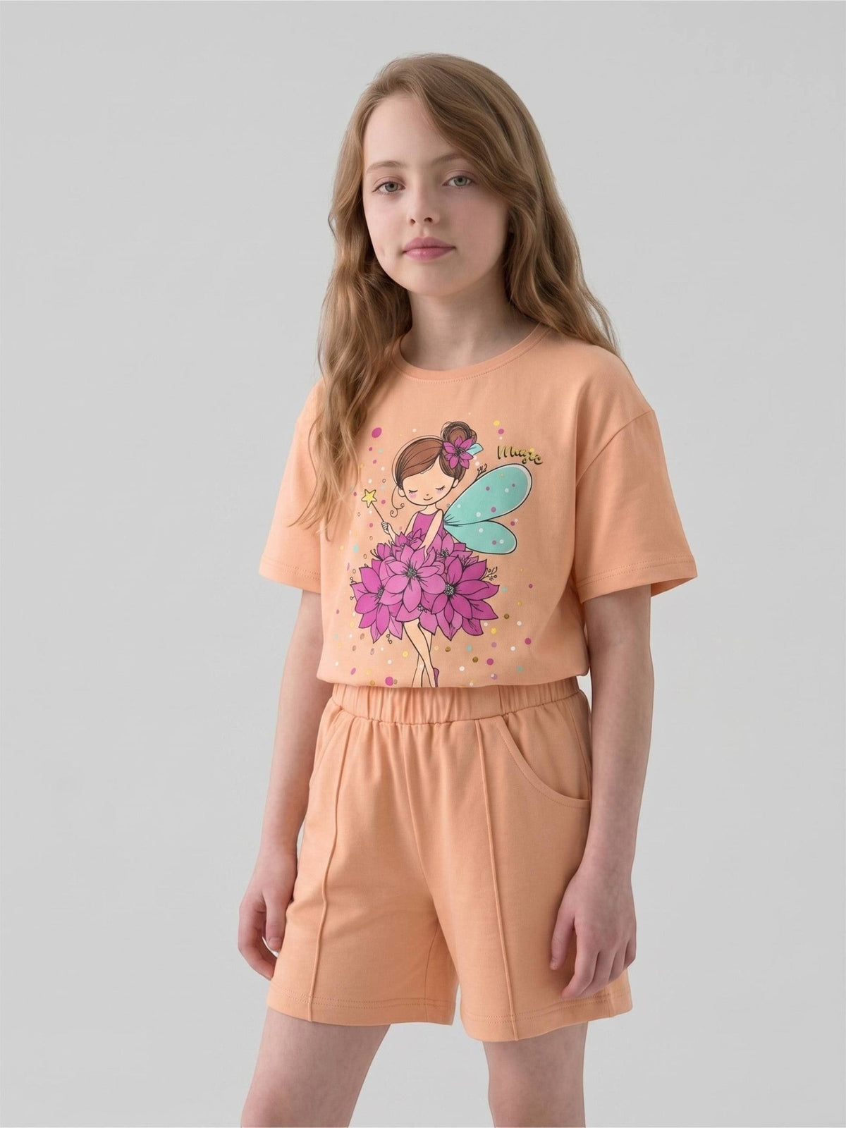 The Nile Luxuries peach graphic t-shirt and shorts set worn by a young girl with a whimsical fairy print design.