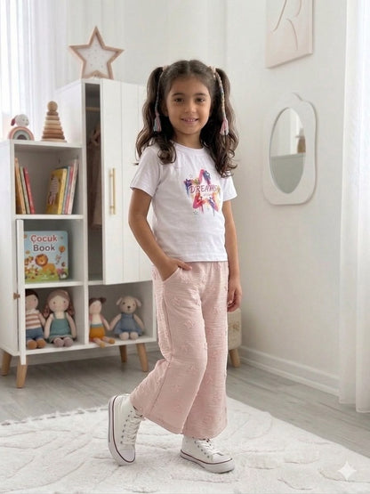 Girl wearing The Nile Luxuries white graphic t-shirt and pink textured wide-leg star pants in a bright playroom.