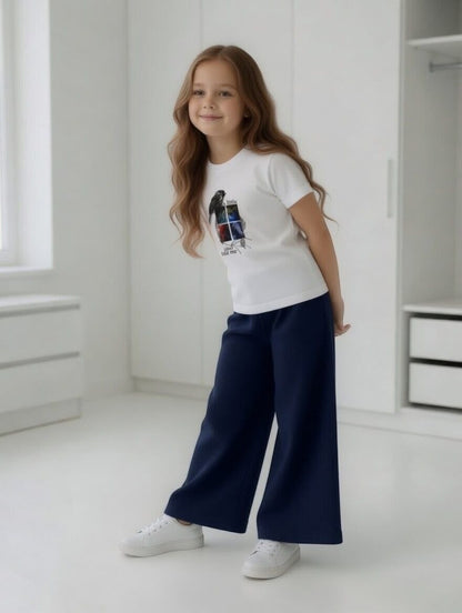 Girl wearing The Nile Luxuries white bird graphic t-shirt and navy blue ribbed wide-leg trousers in a bright room.
