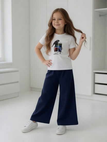 Girl wearing The Nile Luxuries white graphic t-shirt and navy blue ribbed wide-leg trousers in a bright room.