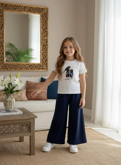 Girl wearing The Nile Luxuries white bird graphic t-shirt and navy blue ribbed wide-leg trousers in a living room.