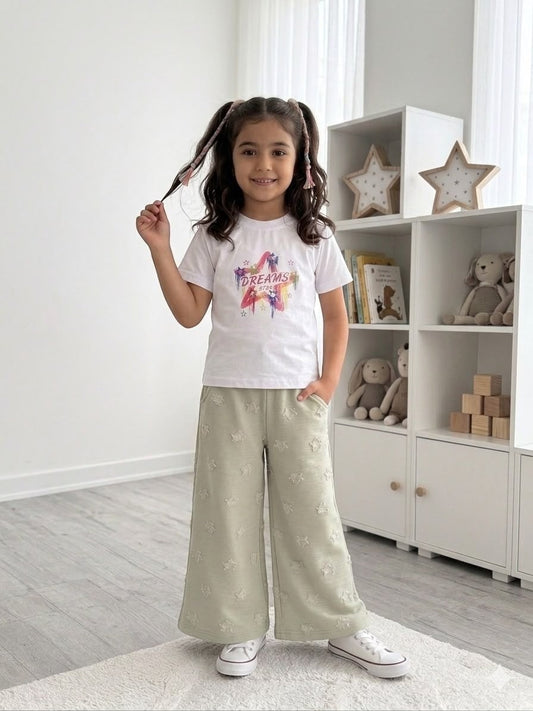 A young girl wearing a The Nile Luxuries white Dreams graphic t-shirt and sage green wide-leg star-patterned pants.