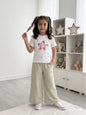 A young girl wearing a The Nile Luxuries white Dreams graphic t-shirt and sage green wide-leg star-patterned pants.