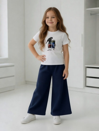 Girl wearing The Nile Luxuries white bird graphic t-shirt and navy blue ribbed wide-leg trousers with white sneakers.