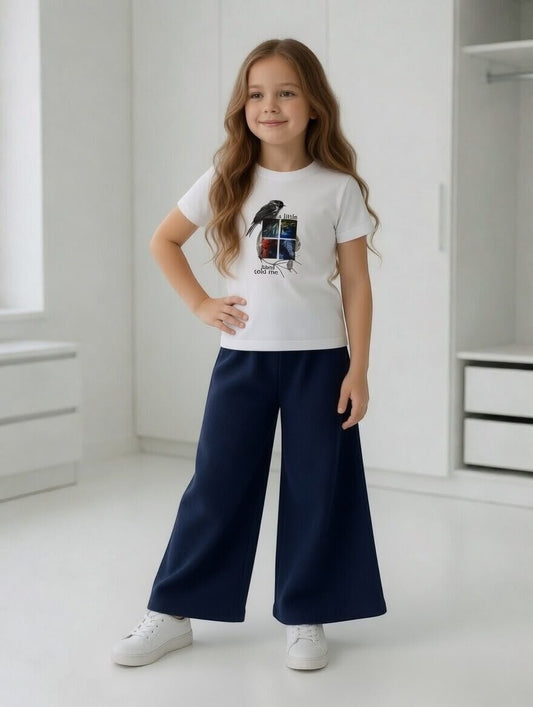 Girl wearing The Nile Luxuries white bird graphic t-shirt and navy blue ribbed wide-leg trousers with white sneakers.