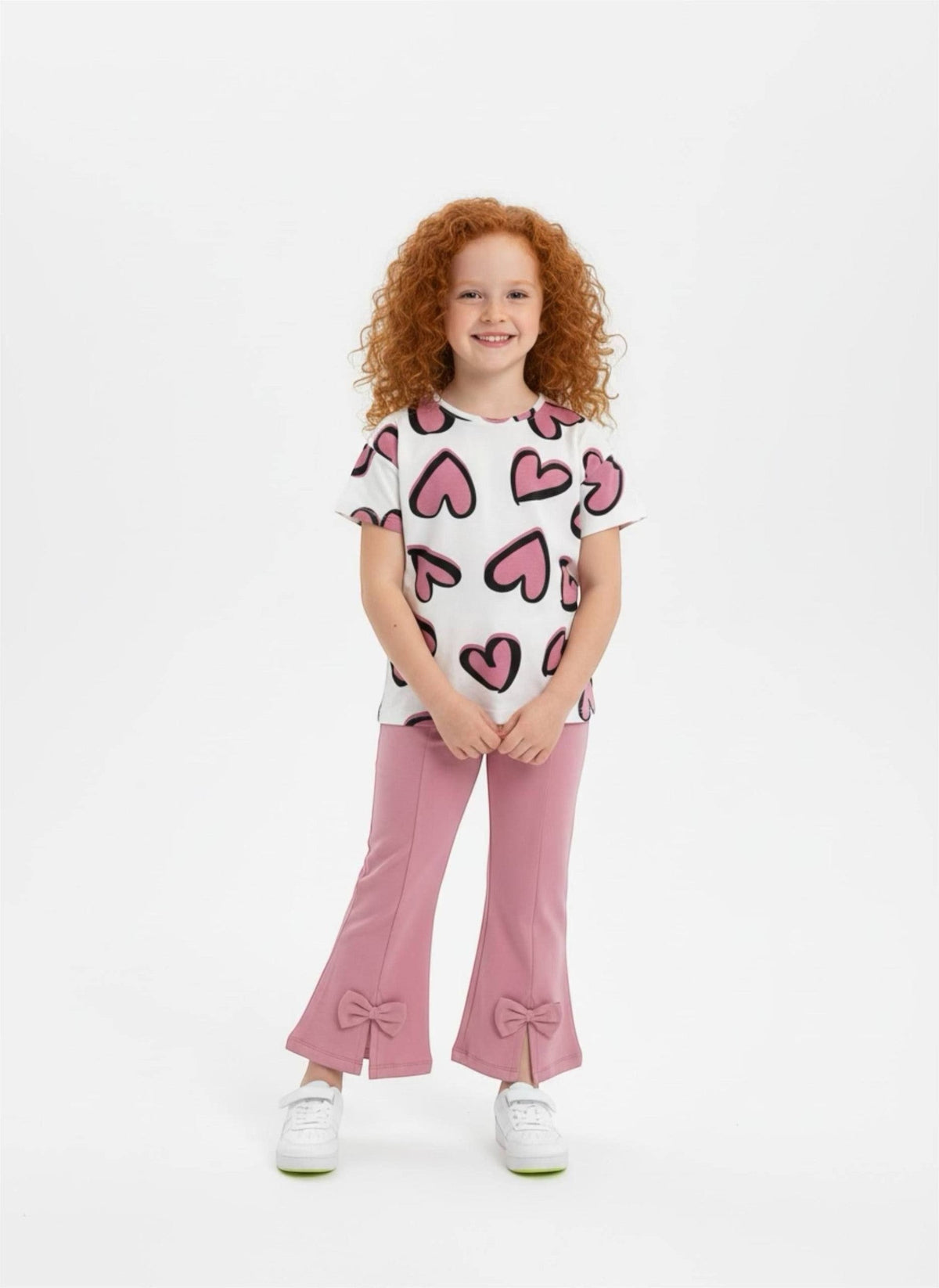 The Nile Luxuries girls set with heart print t-shirt and pink flared trousers featuring bow-accented slit hems.
