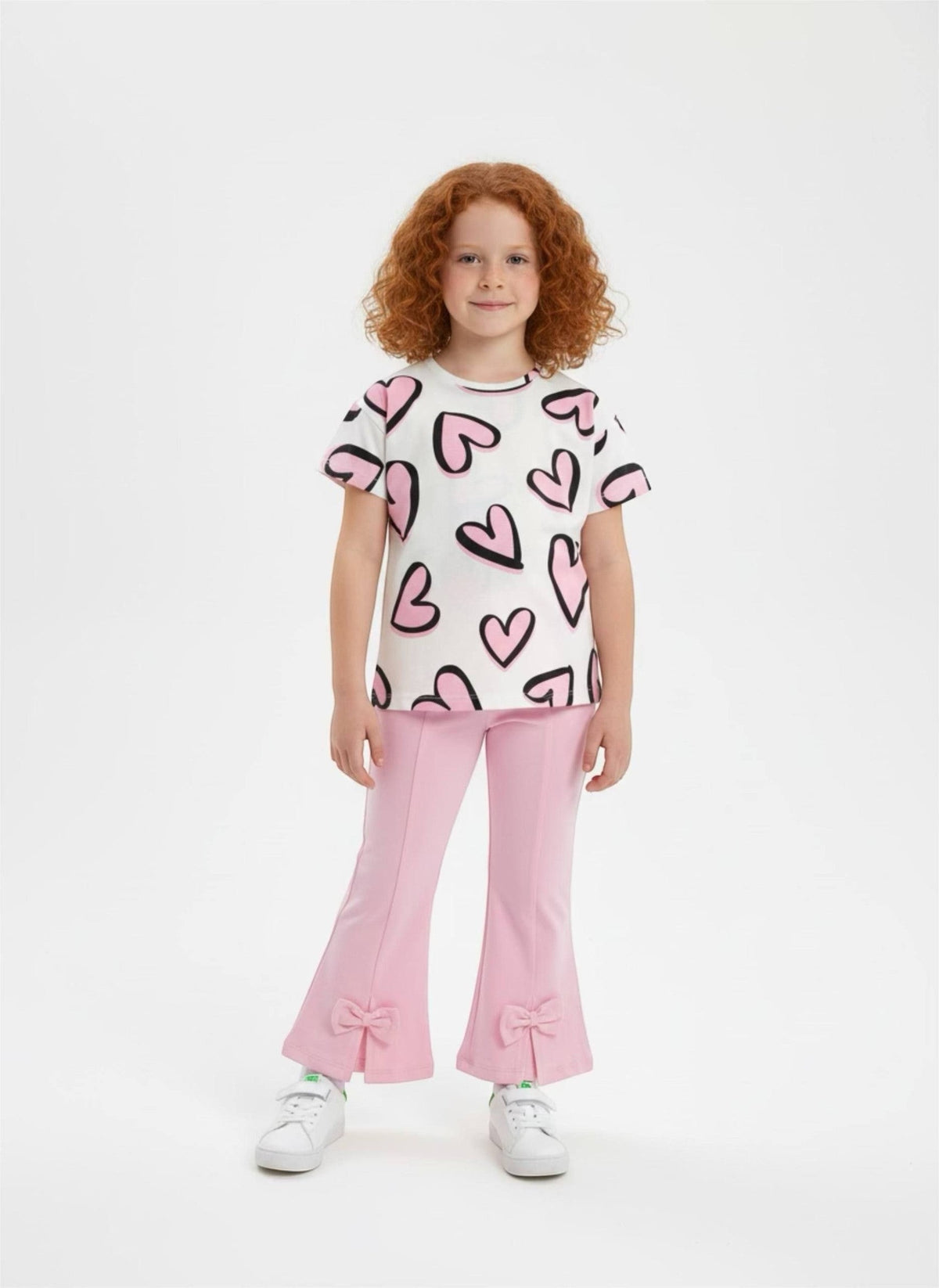 Girl wearing The Nile Luxuries heart print t-shirt and pink flared trousers with bow details on a white background.