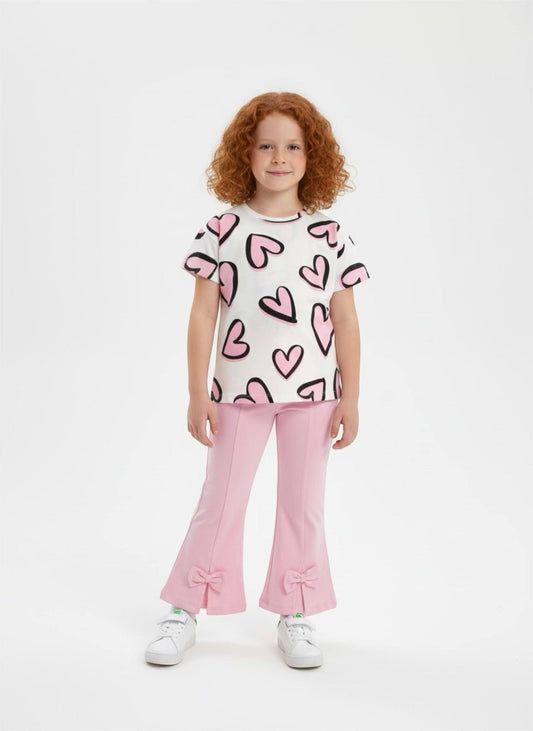 Girl wearing The Nile Luxuries heart print t-shirt and pink flared trousers with bow details on a white background.