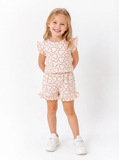 The Nile Luxuries girls' beige lounge set with red heart print, flutter sleeves, and ruffled shorts on a smiling girl.