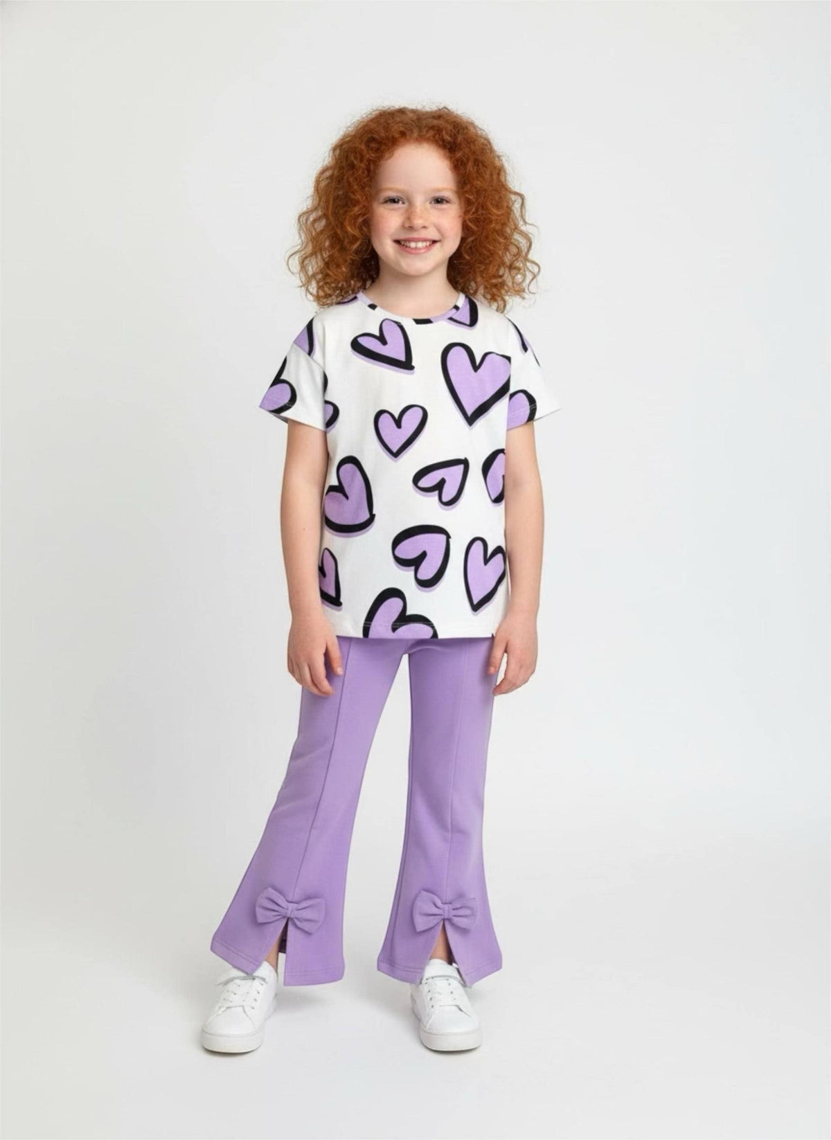 The Nile Luxuries girls' set with heart-print t-shirt and purple flared trousers featuring bow-accented slit hems.