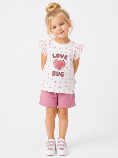 Young girl wearing The Nile Luxuries white heart-print flutter-sleeve t-shirt and pink shorts set.