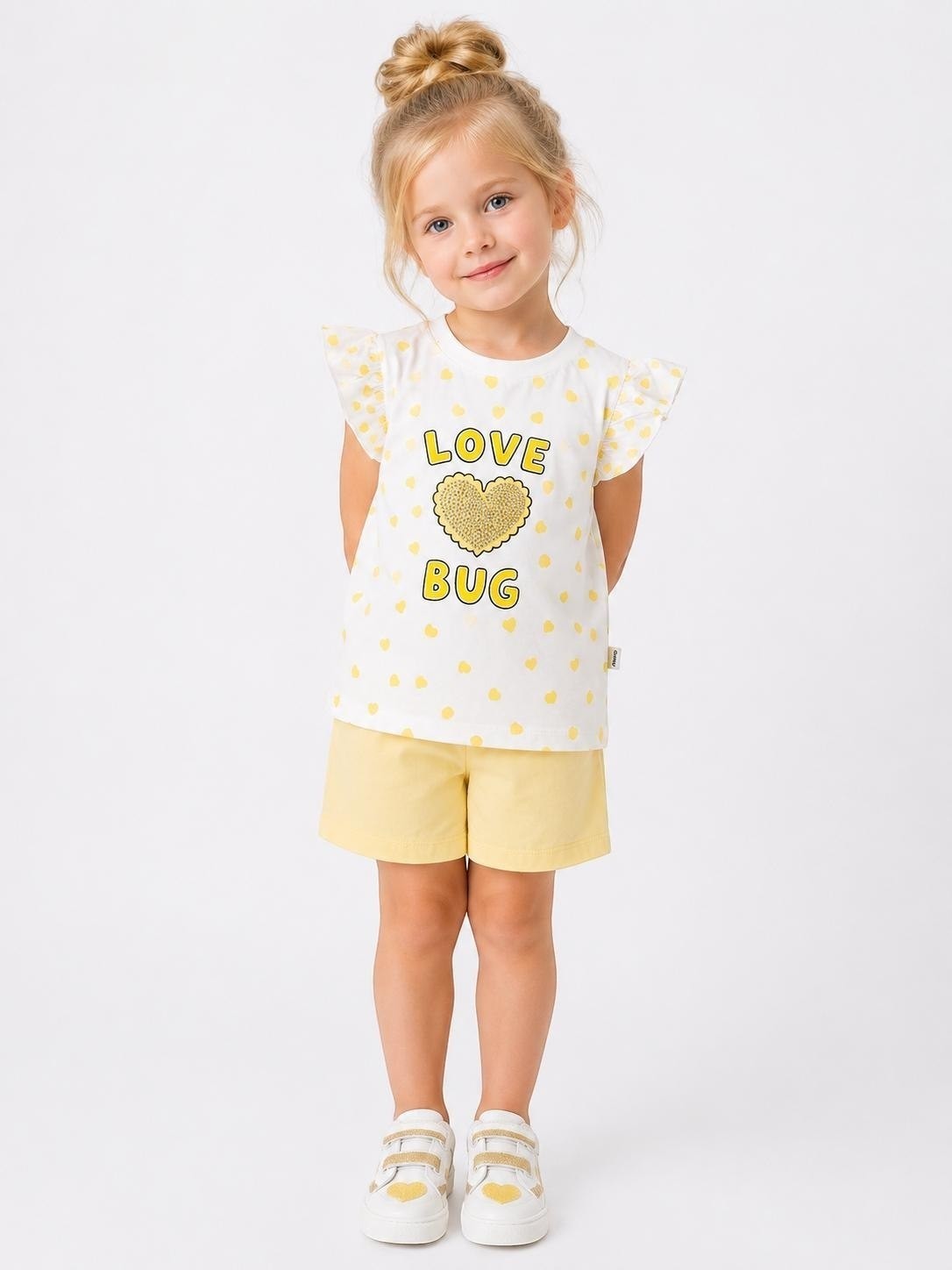 Girl wearing The Nile Luxuries white heart-print flutter-sleeve t-shirt and yellow shorts with Love Bug graphic.