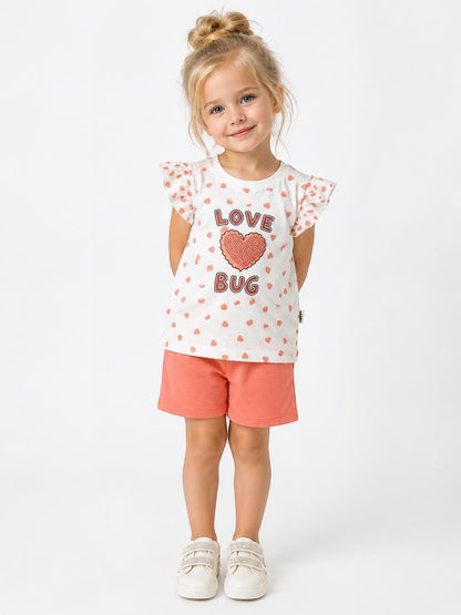 The Nile Luxuries girls heart print t-shirt and coral shorts set with flutter sleeves on a smiling young girl.