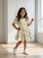 The Nile Luxuries girl wearing a white tiered dress with a yellow lemon and floral print and puff sleeves