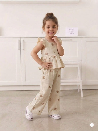 A smiling girl wearing The Nile Luxuries beige muslin floral ruffle peplum top and matching wide-leg trousers.