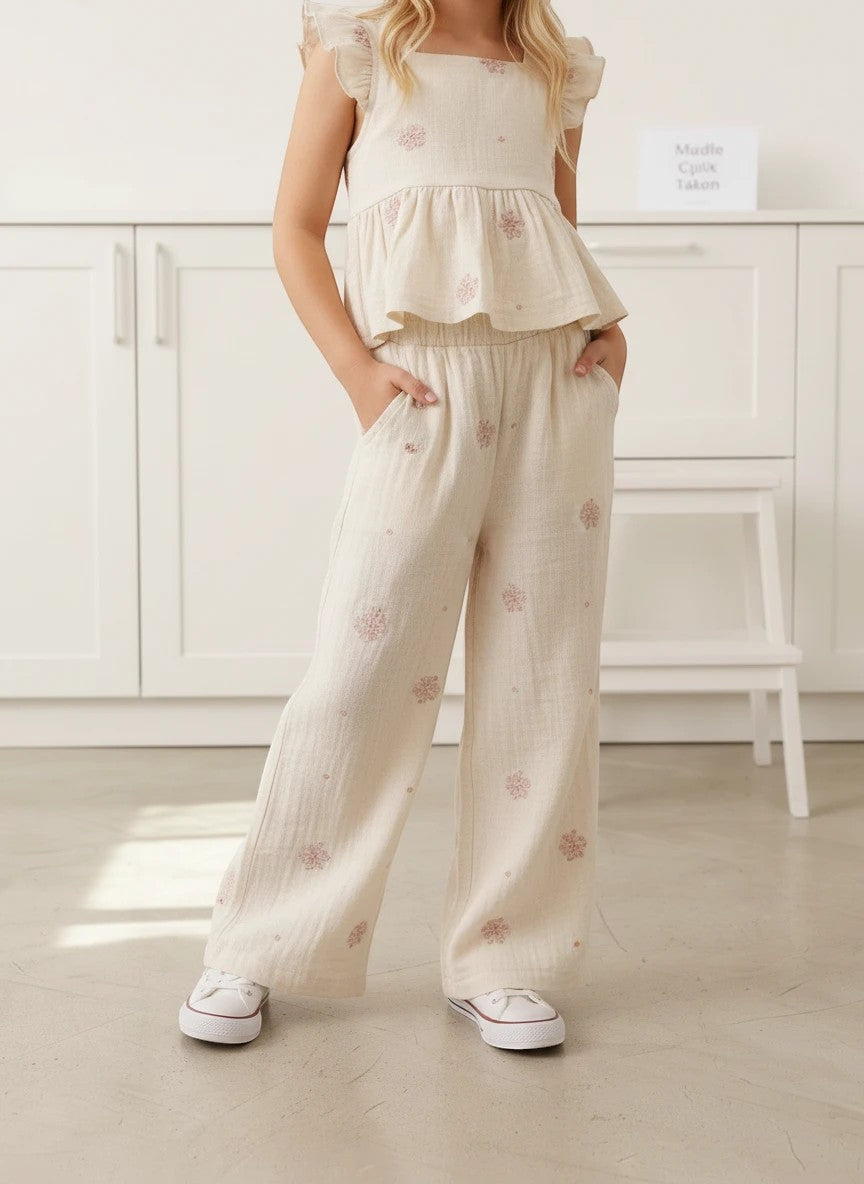 Girl wearing The Nile Luxuries cream muslin ruffle peplum top and matching wide-leg floral pants with white sneakers.