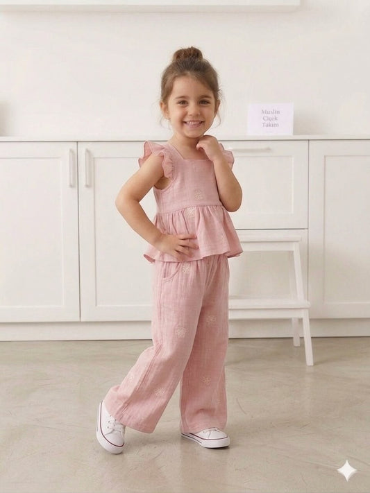A smiling girl wears a pink floral muslin ruffle peplum top and wide-leg pants set by The Nile Luxuries.