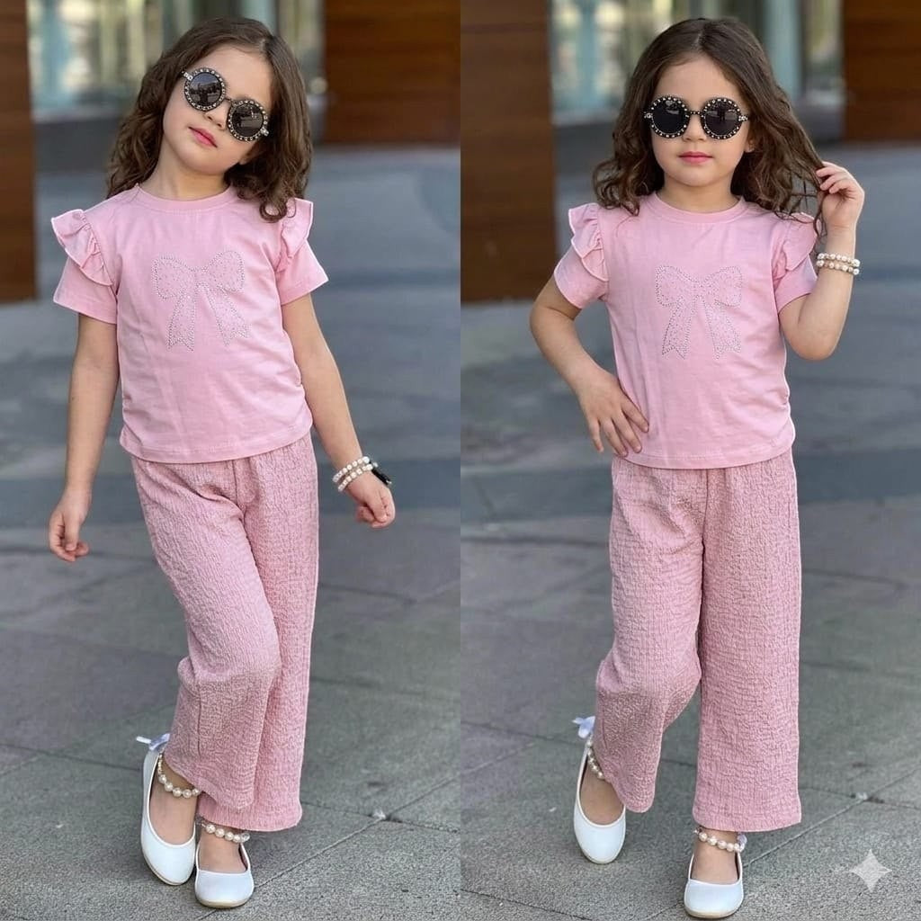 A young girl wearing a pink The Nile Luxuries ruffle sleeve top with a sparkly bow and matching textured trousers.