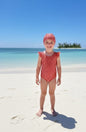 The Nile Luxuries girls red gingham ruffle sleeve swimsuit and matching bonnet on a beach.