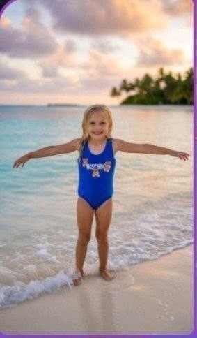 The Nile Luxuries royal blue one-piece swimsuit for girls with a graphic design on the front, worn by a child on a beach.