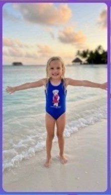 The Nile Luxuries royal blue one-piece swimsuit for girls with graphic design. A young girl stands on a beach.