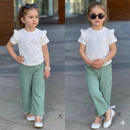 The Nile Luxuries girls set with white flutter-sleeve bow top and green textured trousers on a young model.