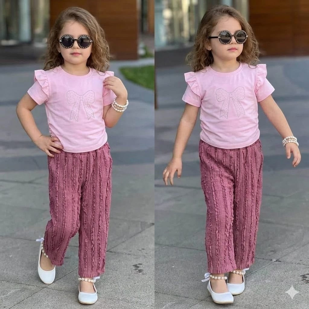 The Nile Luxuries girl's set with pink ruffle-sleeve top, sparkling bow graphic, and mauve textured trousers.