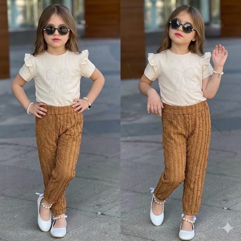 The Nile Luxuries girls' outfit with a cream ruffle-sleeve bow t-shirt and brown textured trousers, worn by a child.