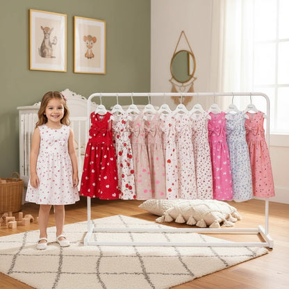 A young girl standing next to a clothing rack displaying The Nile Luxuries sleeveless A-line dresses with bow details.