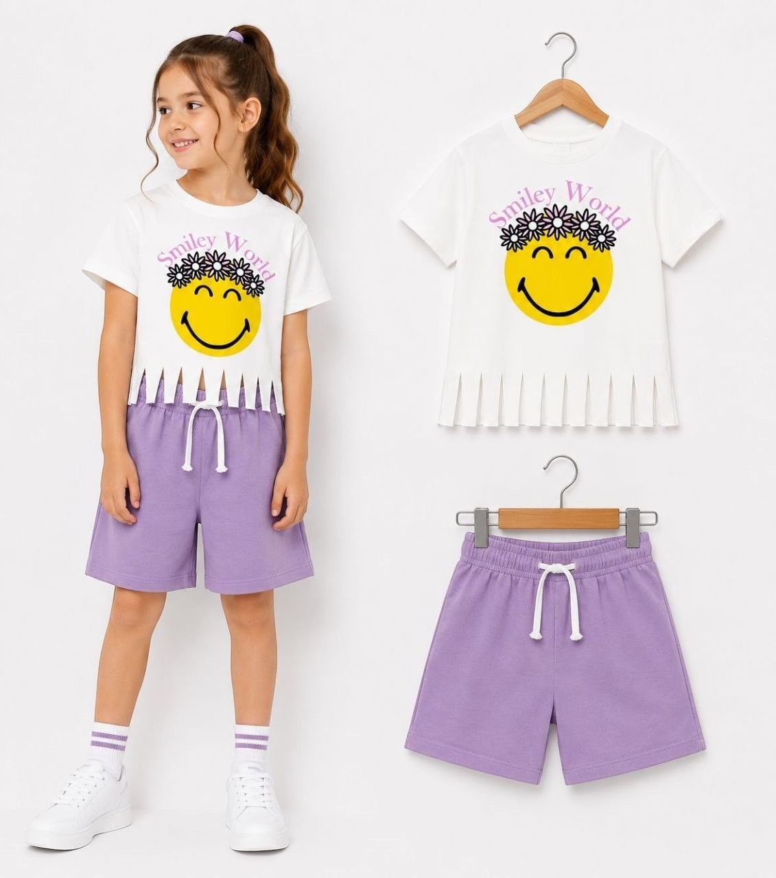 The Nile Luxuries girls' white t-shirt with smiley face graphic and floral crown, paired with lilac shorts. Fringed hem detail.