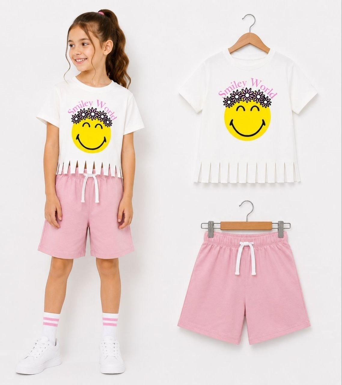 The Nile Luxuries white t-shirt with smiley face graphic and pink shorts set for girls. T-shirt has floral crown and fringed hem. Shorts have elastic waist and drawstring.