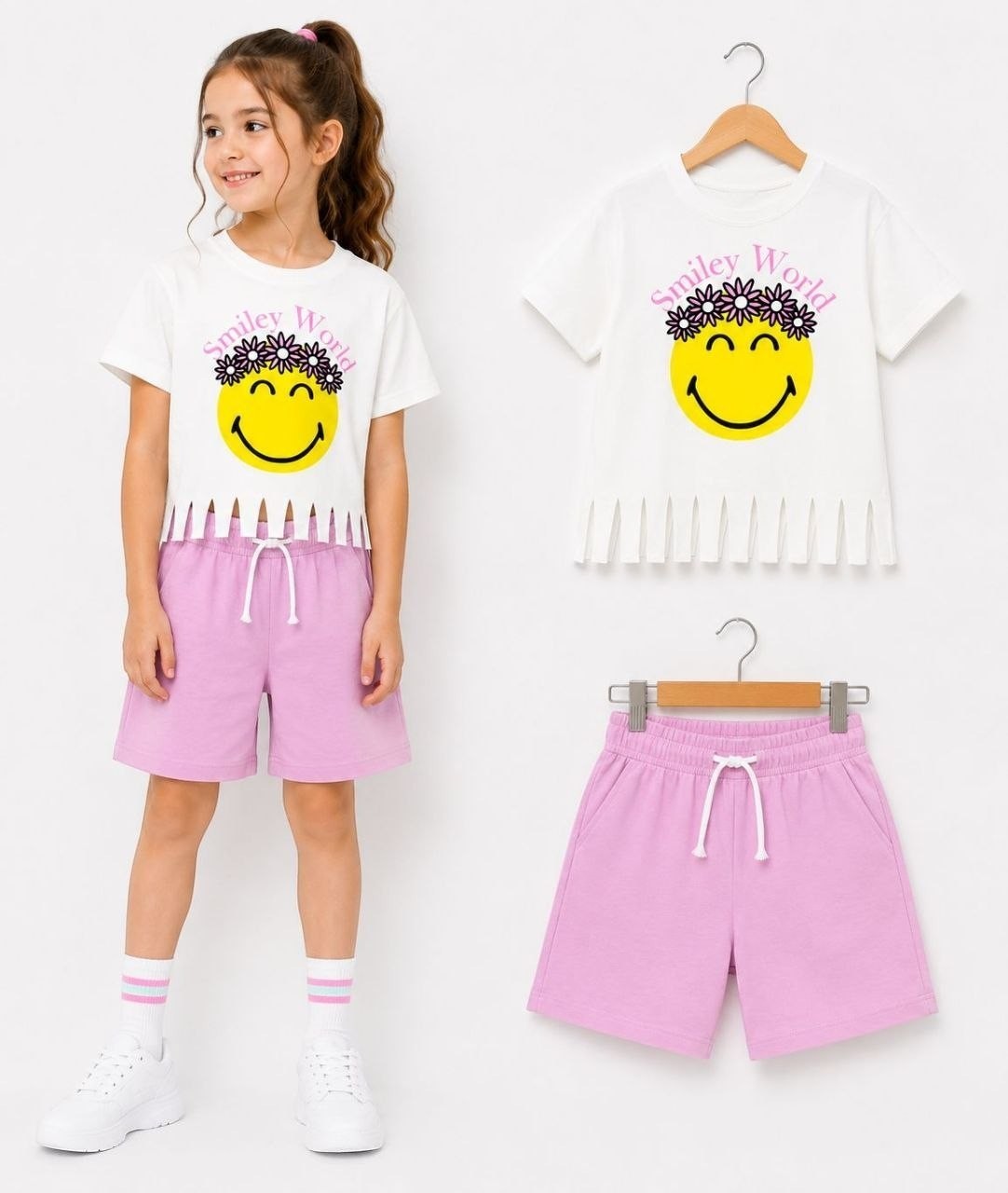 The Nile Luxuries girls' white t-shirt with smiley face graphic and fringed hem, paired with lilac shorts. Casual set.