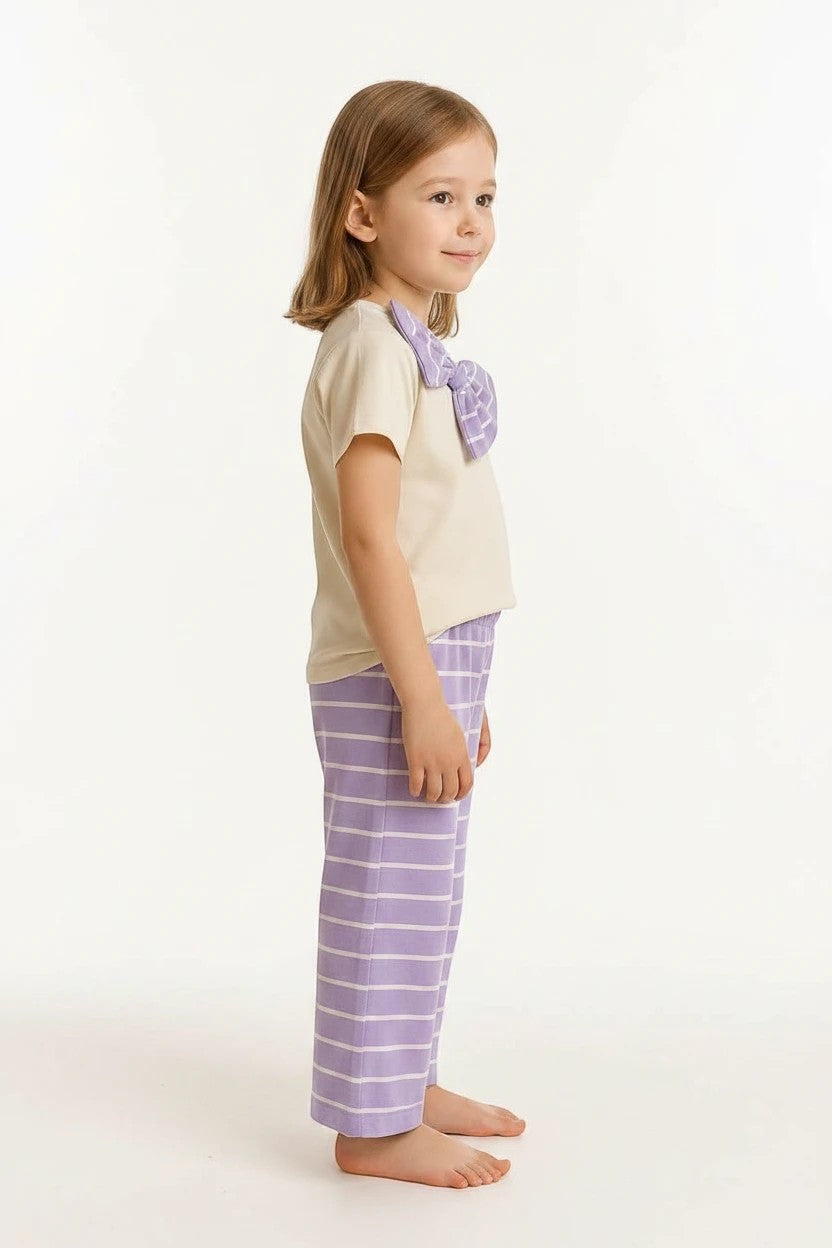 The Nile Luxuries girls pajama set with a cream top, purple bow detail, and striped wide-leg pants on a young girl.