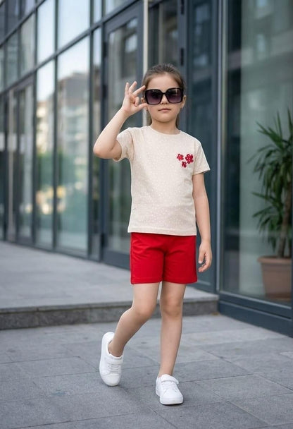 Girl wearing The Nile Luxuries polka dot t-shirt with floral appliqué and red shorts with white sneakers outdoors.