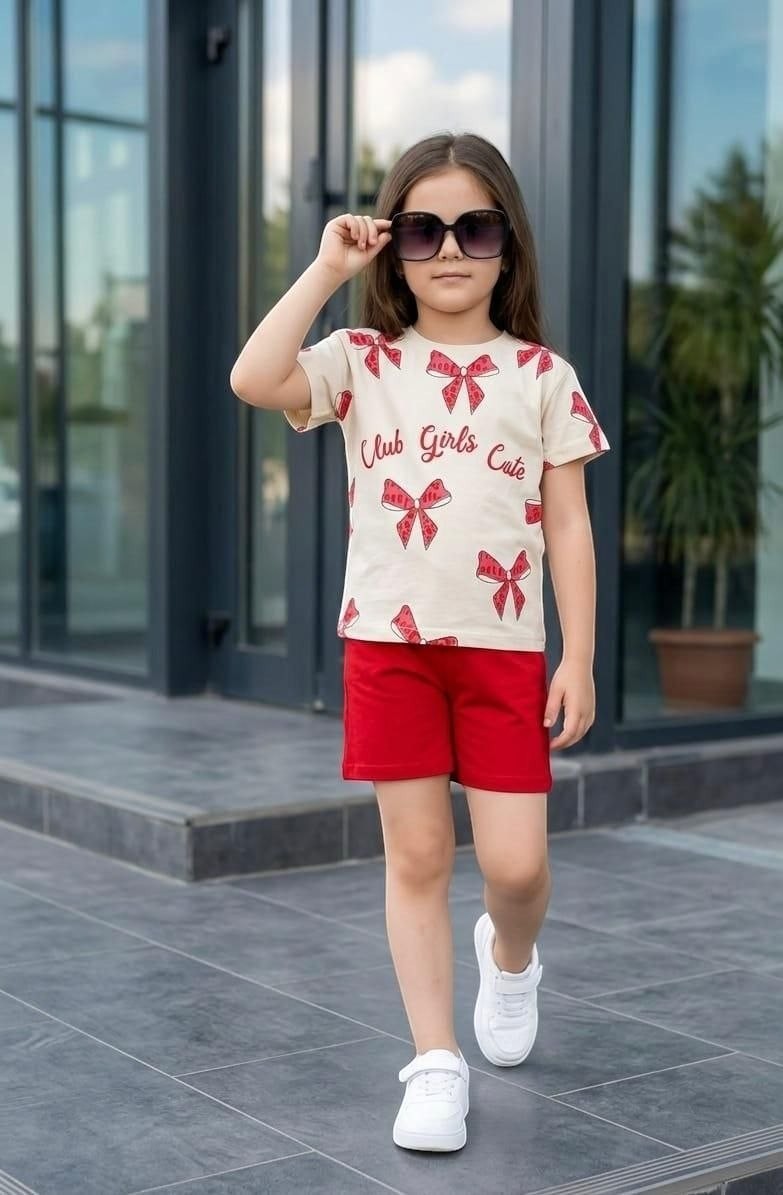 The Nile Luxuries girls' summer set with a cream bow-print t-shirt and red shorts, worn by a girl with sunglasses.