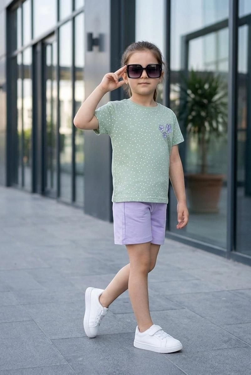 Young girl wearing The Nile Luxuries sage green polka dot t-shirt with floral appliqué and lilac shorts with white sneakers