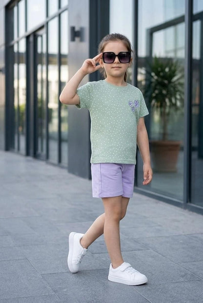 Young girl wearing The Nile Luxuries sage green polka dot t-shirt with floral appliqué and lilac shorts with white sneakers