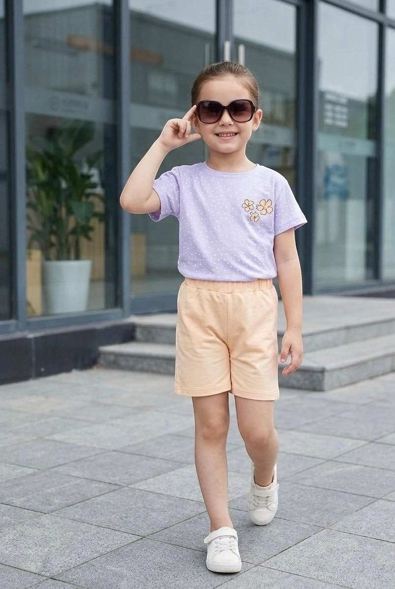 Young girl wearing The Nile Luxuries lavender polka dot t-shirt with floral appliqué and peach shorts outdoors.