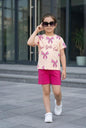 The Nile Luxuries girls' summer set with peach bow-print t-shirt and pink shorts, worn by a girl in sunglasses.